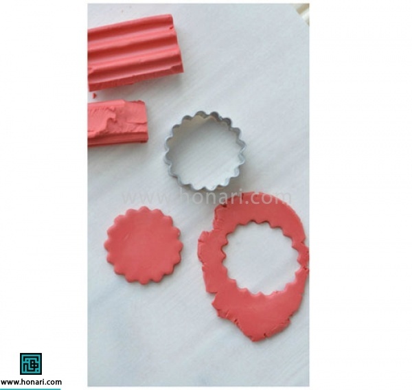 آموزش گوشواره خمیری با طرح شیرینی ماکارون-مرحله 1 ابتدا دایره کوچکی را از خمیر فیمو جدا کرده و آن را با استفاده از وَردَنِه کمی پهن میکنیم . سپس با استفاده از قالب دالبری قسمتی از آن را جدا میکنیم