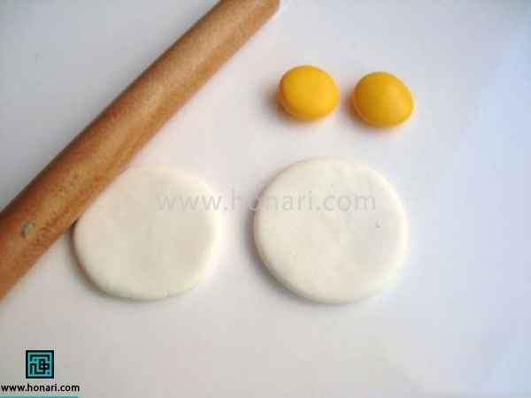آموزش گوشواره خمیری با طرح گل-مرحله 2 با استفاده از وردنه دایره های سفید را صاف میکنیم. دقت کنید که باید هر دو به یک اندازه باشند. دایره های زرد را نیز کمی صاف میکنیم