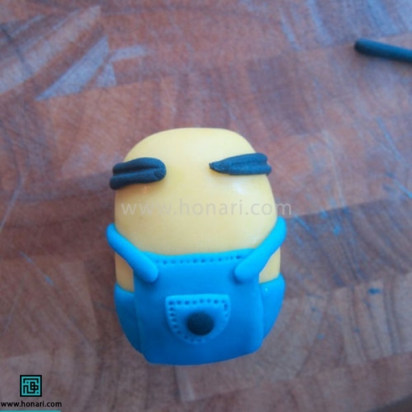 آموزش عروسک خمیری مینیون-مرحله 12 مانند تصویر آن را دور سر میپیچیم . دقت کنید قسمت وسط جلوی سر عروسک خمیریرا برای چشم خالی بگذارید