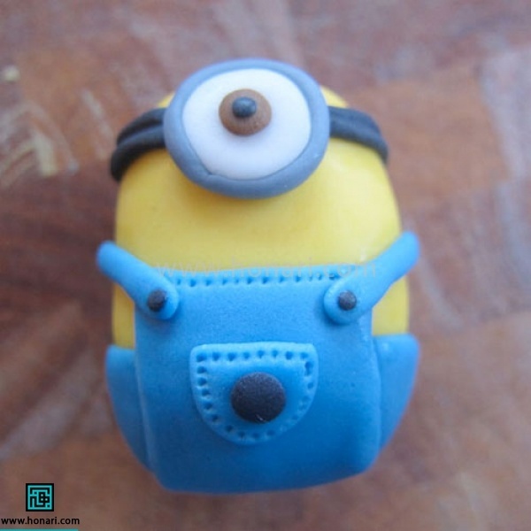 آموزش عروسک خمیری مینیون-مرحله 15 یک دایره مشکی به عنوان دکمه جیب و دو دایره کوچکتر به عنوان دکمه کمربند شلواردرست کرده در جای خود وصل میکنیم.