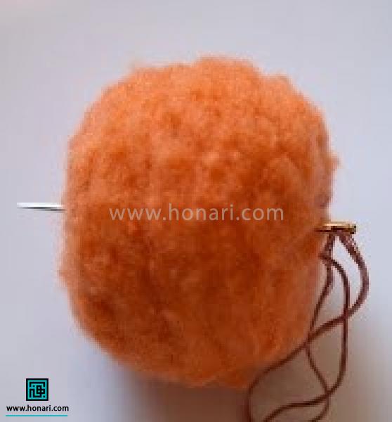 آموزش ساخت کدو تنبل با الیاف کچه دوزی-مرحله 4 با استفاده از نخ و سوزن مثل تصاویر به توپک فرم دهید از وسط توپک سوزن و نخ را وارد کرده.