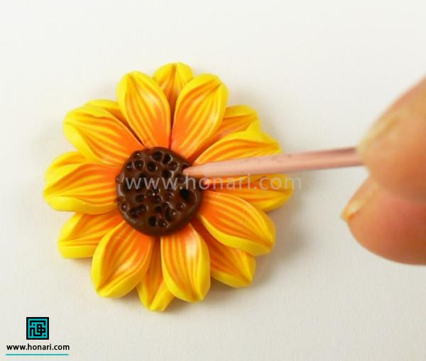 آموزش ساخت گل آفتابگردان با خمیر فیمو-مرحله 19 درآخر باز در مرکز گل یه دایره ی قهوه ای دیگه قرار میدیم و به کمک یه شی نوک تیزجای تخمه آفتابگردونها رو مشخص میکنیم.