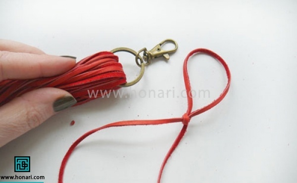 اموزش ساخت آویز چرمی -مرحله 6 ابتدا و انتهای تریشه ها را روی هم قرار میدهیم . سپس توسط نخ دیگری حلقه ای با دنباله بلند درست میکنیم. (بهتر است گره حلقه مانند گره کروات باشد )