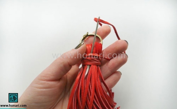 اموزش ساخت آویز چرمی -مرحله 8 حال مابقی نخ را دور تریشه ها محکم می پیچیم و در آخر با سوزن آن را از زیر عبور میدهیم تا گره محکم شود.