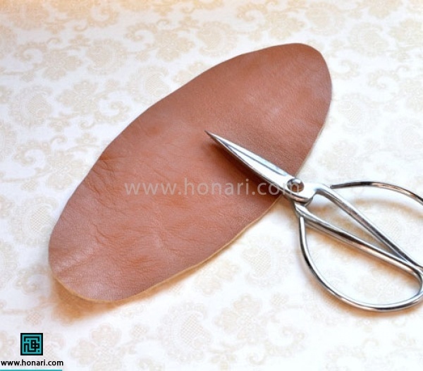 موادو ابزار اولیه مورد نیاز برای شروع آموزش چرم دوزی : چرم مصنوعی ، دکمه چهار پارچه طرح دار ، چسب اهن ، دکمه زن میانه ، قیچی چرم بیضی به اندازه 22 در 10 سانتی متر از چرم برش میزنیم.( با توجه به اندازه دور مچ دستان این اندازه میتواند تغییر کند) 