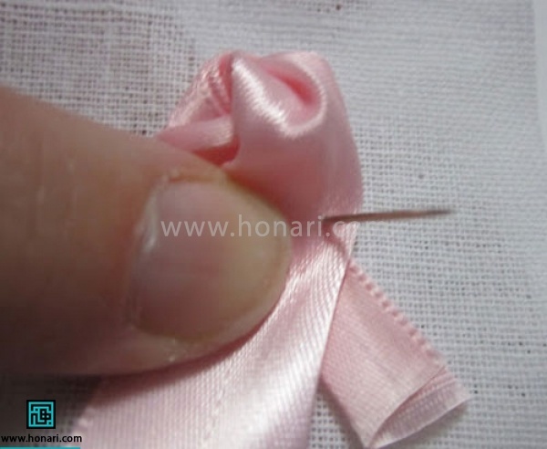 یک دور ادامه روبان را دور گره ایجاد شده بزنید و با نخ و سوزن به پارچه وصل کنید