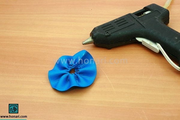 نخ جمع شده را در انتها گره بزنید و دو سر روبان را با چسب تفنگی به هم وصل کنید تا شکل یک گل بگیرد
