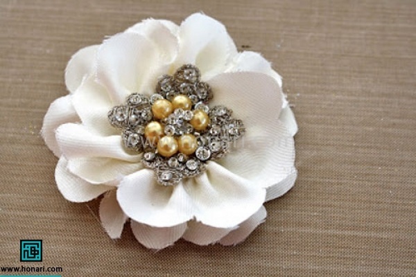 با چسب تفنگی روبان را ثابت کنید تا از هم باز نشود. با سنگ و نگین در مرکز کار دوخت گل به اتمام میرسد